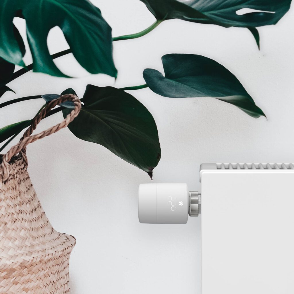 Tado-radiatorknop op een witte radiator naast een kamerplant