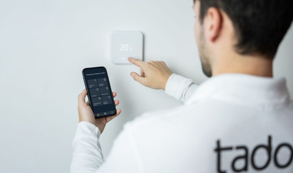 Persfoto van een Tado-thermostaat en een telefoon met installateursapp
